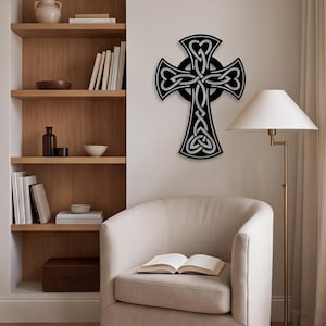 Könnte beinhalten: Ein schwarzes, an der Wand montiertes keltisches Kreuz mit komplizierten, durchgehenden Knotenmustern und hellgrauen Umrandungen. Das Kreuz hat eine kreisförmige Mitte und vier ausgestellte Arme, die jeweils in einem herzförmigen Design enden.