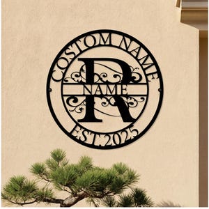 May include: Black metal custom name sign with a circular design. The sign features the text "CUSTOM NAME" around the outer edge, with a large letter "R" and the word "NAME" in the center. The year "EST 2025" is at the bottom.