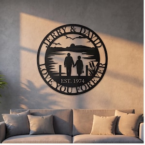 May include: Black metal wall art featuring a circular design with the names "Jerry & David" and the phrase "Love You Forever." The artwork depicts a couple holding hands by a lake, with the year "EST. 1974" below. The art is mounted on a neutral-colored wall.