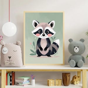 Könnte beinhalten: Gerahmte Aquarellillustration eines Waschbären mit hellgrünem Hintergrund. Der Waschbär hat einen grau-braunen Kopf, einen schwarz-grauen Körper und einen gestreiften Schwanz. Rosa Rouge akzentuiert die Wangen. Das Kunstwerk wird auf einem weißen Regal mit Spielzeug und Büchern ausgestellt.