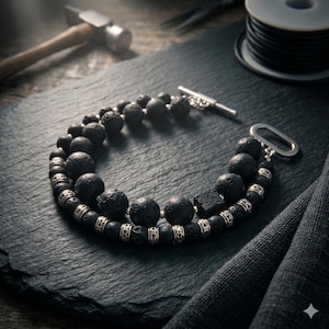 May include: A double-strand bracelet made with black lava stone beads and silver-coloured metal details. The bracelet has a silver clasp. The jewellery is presented on a dark, textured surface.