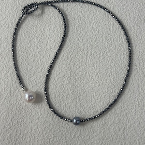May include: A delicate necklace featuring a strand of small, dark gray beads. The necklace has two prominent pearls: one white and one gray. The design is simple and elegant, suitable for various occasions.