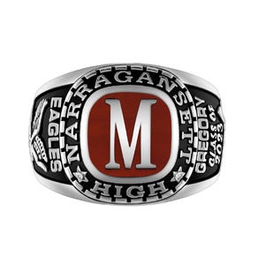 May include: A silver-coloured class ring with a black band. The ring features the word "Narragansett" and "Eagles" on the sides. The centre has a red background with a white "M" and the words "Gregory" and "Class of 2023".