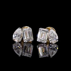 Puede incluir: Un par de pendientes de botón engastados en oro amarillo, cada uno con una combinación de una piedra preciosa transparente de corte esmeralda y una piedra transparente de corte de pera. Las piedras están facetadas y reflejan la luz.