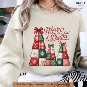 May include: A beige sweatshirt with a Christmas-themed design. It features three patchwork Christmas trees in red, green, and white, decorated with bows and snowflakes. The words "Merry & Bright" are written in red script.