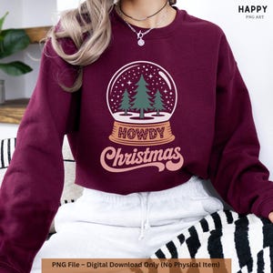 May include: A burgundy sweatshirt with a snow globe design. The design includes three green Christmas trees, stars, and the words "HOWDY Christmas." The text "PNG File - Digital Download Only (No Physical Item)" is at the bottom of the image.