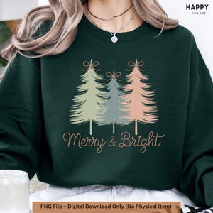 May include: A dark green sweatshirt with a festive design. It features three pastel-coloured Christmas trees and the words "Merry & Bright" in a cursive font. A seasonal, holiday-themed garment.
