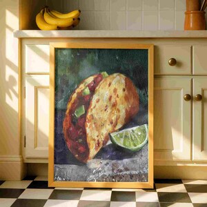 May include: A framed painting of a taco with a lime wedge. The taco has a golden-brown shell, filled with red and green ingredients. The lime is a vibrant green. The frame is a light wood color.