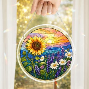 Pu&ograve; includere: Opera d'arte circolare in vetro colorato con un girasole, margherite e lavanda in un campo con un tramonto. L'opera &egrave; tenuta da una catena d'argento e ha un bordo trasparente.