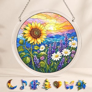 Pu&ograve; includere: Un puzzle rotondo in stile vetrata raffigurante un girasole, margherite e lavanda sullo sfondo di un tramonto. Il puzzle &egrave; esposto in una cornice trasparente e circolare con una catena per appenderlo. Ulteriori pezzi del puzzle sono mostrati sotto.