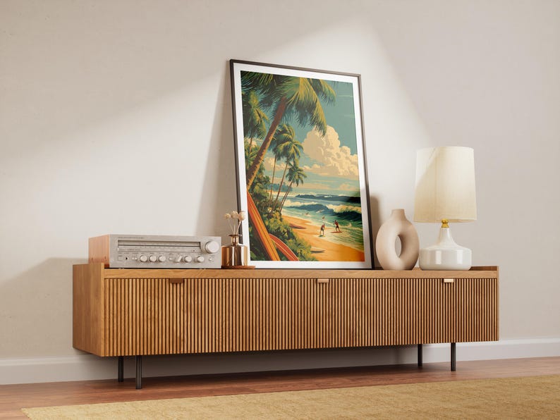 May include: A framed art print depicting a tropical beach scene with palm trees, surfers, and waves. The artwork is displayed on a wooden cabinet with a vintage stereo, a vase, and a lamp.