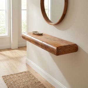 Puede incluir: Estante de madera montado en la pared con un acabado marrón cálido. Un plato pequeño y de color claro se encuentra en el estante. Un espejo redondo con marco de madera está encima del estante. El estante mide aproximadamente 122 cm de largo.