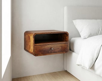 Könnte beinhalten: Ein wandmontierter, schwebender Nachttisch aus dunkelbraunem Holz mit einem glatten, abgerundeten rechteckigen Rahmen. Das Möbelstück verfügt über ein offenes oberes Ablagefach und eine einzelne untere Schublade mit einem kleinen, mittigen Metallknopf.