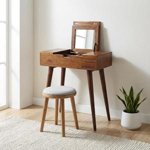 May include: A mid-century modern vanity set with a flip-top mirror, a drawer, and tapered legs. The vanity is made of dark wood and includes a round stool with a gray upholstered seat. A potted plant sits nearby.