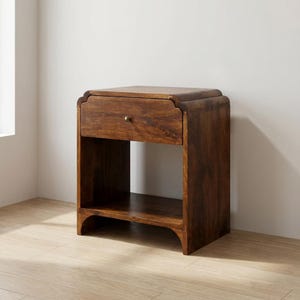 May include: A dark brown wooden nightstand with a single drawer and an open shelf. The nightstand has a curved top and a brass knob on the drawer. The wood grain is visible, and the piece has a warm, inviting appearance. The nightstand is a bedroom furniture item.