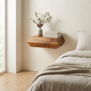 Può includere: Mensola galleggiante in legno geometrica, di colore marrone caldo, con un piccolo vaso con foglie secche e una pila di libri. La mensola è montata su una parete neutra, creando un design minimalista. Misura circa 60 cm di lunghezza.