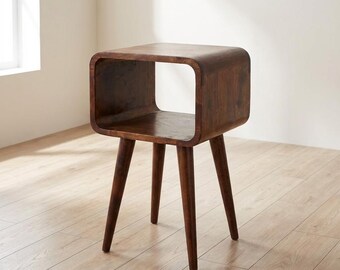 May include: A dark brown wooden side table featuring a smooth, rounded rectangular top section with an open storage compartment. The piece is supported by four tapered, angled legs that extend outward from the base of the main structure.