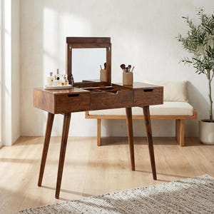 May include: A dark brown wooden vanity table featuring a flip-top mirror, two side drawers, and a central storage compartment. The piece stands on four tapered legs and includes a small tray with glass bottles and a woven cup holding makeup brushes.