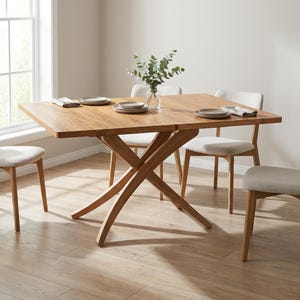 Peut inclure: Une table à manger en bois clair avec un piètement en forme de X, garnie d'assiettes, de serviettes et d'un vase de verdure. Quatre chaises de couleur claire entourent la table, créant un espace repas chaleureux.