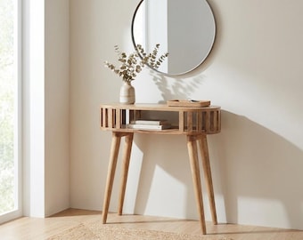 Könnte beinhalten: Ein heller Holzkonsolentisch mit vier konisch zulaufenden Beinen und einem offenen Regal mit Lamellenstruktur. Die glatte Tischplatte trägt eine Keramikvase mit getrockneten Eukalyptuszweigen und ein kleines rechteckiges Flecht-Tablett.