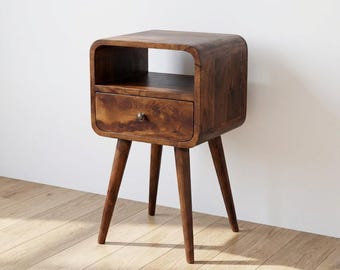 May include: A dark brown wooden bedside table featuring a rounded rectangular frame with an open storage shelf at the top and a single drawer below. The piece is supported by four tapered, angled legs and includes a small, round metal drawer knob.