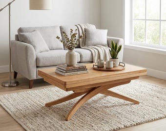 May include: A light wood lift-top coffee table with a rectangular surface and curved legs. The table holds a stack of three books, a textured ceramic vase with eucalyptus branches, and a wooden tray with two ceramic mugs and a small potted plant.