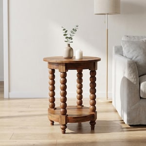 May include: A round wooden side table featuring a smooth tabletop and a lower shelf supported by four legs composed of stacked wooden spheres. The table has a medium brown finish and is positioned on a light-colored wooden floor.