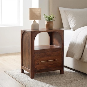 May include: A dark brown wooden nightstand featuring an arched open top shelf and a single lower drawer with a thin horizontal gold handle. The nightstand is topped with a beige lamp and a small green potted plant in a terracotta-colored pot.