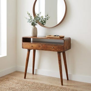 May include: A mid-century modern wooden console table with two drawers and tapered legs. A round mirror hangs above the table, and a vase with greenery sits on top. The table is approximately 76 cm wide.