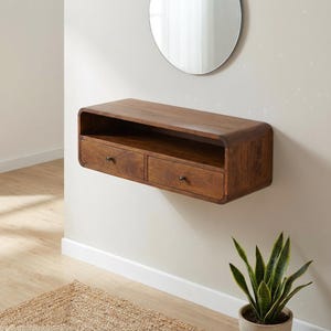 Peut inclure: Étagère murale en bois brun chaud avec deux tiroirs et une étagère supérieure ouverte. L'étagère est fixée à un mur blanc. Les tiroirs ont de petits boutons foncés. Un miroir rond est au-dessus.