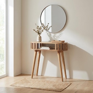 May include: A light-colored wooden console table with a round top and four angled legs. A round mirror hangs above the table. A small rug is on the floor in front of the table. A vase with dried flowers sits on the table.