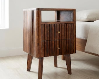 May include: A dark brown wooden bedside table featuring a vertical slatted design on the sides and two drawers. The piece includes an open storage shelf at the top and is supported by four tapered legs. Each drawer is accented with a small brass knob.