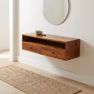May include: A floating wooden console with two drawers and a shelf, finished in a warm brown tone. A small bowl and keys rest on top. A round mirror hangs above the console, and a woven rug lies on the floor.