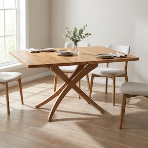 Puede incluir: Una mesa de comedor de madera marrón claro con tablero rectangular y base de patas cruzadas, acompañada de cuatro sillas con asientos tapizados en color beige claro. Un jarrón de cristal transparente con eucalipto en el centro.
