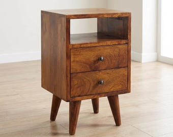 May include: A brown wooden bedside table featuring an open top shelf and two drawers, each fitted with a single dark metal knob. The piece is supported by four tapered legs and displays a visible wood grain pattern throughout its structure.