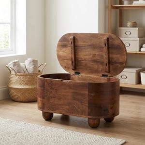 Op de afbeelding: Een middelbruine houten opbergkist met een afgeronde ovale vorm, voorzien van een scharnierend deksel dat openstaat. De kist rust op vier korte, ronde pootjes en heeft een natuurlijke houtnerfafwerking over het gehele buitenoppervlak.