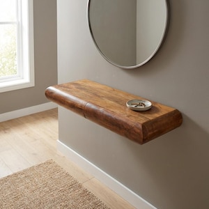 Puede incluir: Estante de madera flotante con borde curvo, montado en una pared gris. Un plato pequeño y redondo con llaves descansa sobre el estante. Un espejo redondo con marco plateado está encima. El estante es de madera de tono cálido.