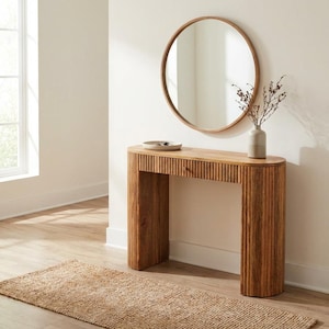 May include: A light brown wooden console table with a fluted texture on the front and sides, featuring a single drawer. Above the table hangs a round mirror with a matching light brown wooden frame. A ceramic vase with dried branches sits on top.