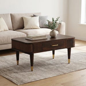 Peut inclure: Une table basse rectangulaire en bois brun foncé dotée d'un tiroir central avec une poignée dorée, de coins arrondis et de panneaux latéraux en cannage tressé. La table repose sur quatre pieds fuselés avec des embouts métalliques dorés.