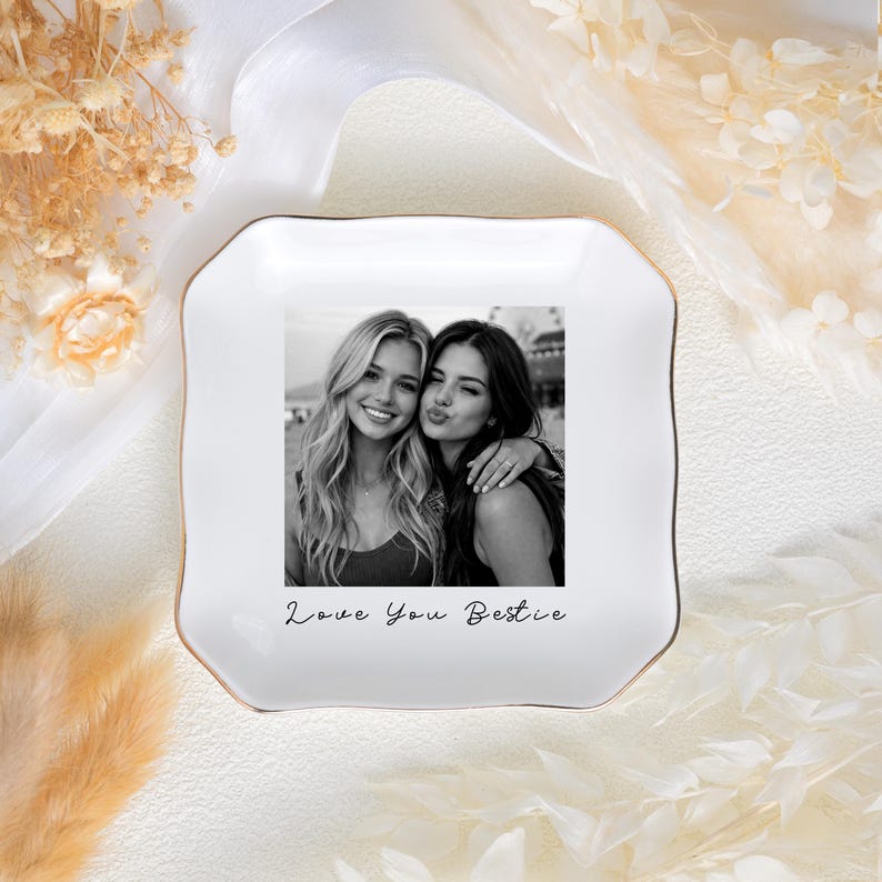 May include: White ceramic trinket dish with a gold rim, featuring a black and white photo of two smiling women. The dish has the inscription "Love You Bestie" in script.