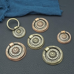 May include: A selection of antique-style drawer pulls and handles in various sizes. The hardware features a central floral design, surrounded by decorative rings and a variety of metallic finishes, including bronze, copper, and brass. Some pulls have a ring handle.