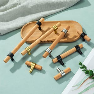 May include: A collection of wooden cabinet pulls with metal accents in black, gold, and silver. The pulls have a cylindrical wooden handle and are displayed on a wooden tray. The text "PerfecCrafts" is visible on the tray.