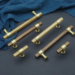 May include: A collection of wooden cabinet pulls with brass hardware. The pulls feature a rectangular wooden center section and rounded brass ends. The wood tones vary from light to dark brown. The pulls are arranged on a dark surface.