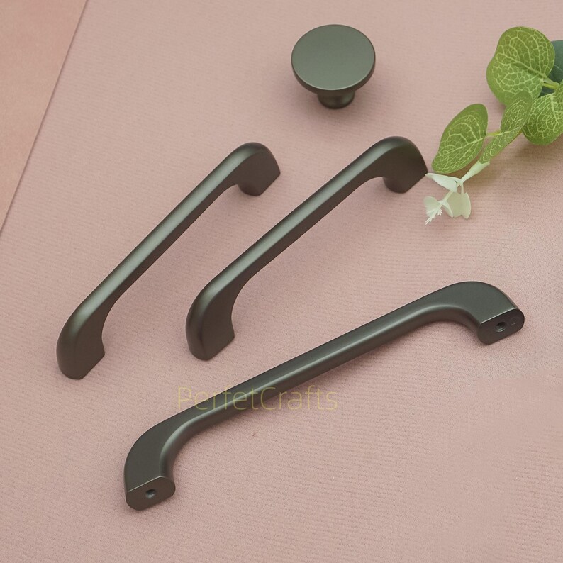 Op de afbeelding: Een set grijze kastbeslag, waaronder drie handgrepen en een ronde knop. De handgrepen hebben een gebogen ontwerp en zijn gemaakt van mat metaal. De tekst "PerfetCrafts" is zichtbaar op de onderste handgreep.