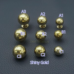 Puede incluir: Una colecci&oacute;n de pomos dorados brillantes para armarios de varios tama&ntilde;os. Los pomos tienen un dise&ntilde;o esf&eacute;rico con un v&aacute;stago y una base. El texto "Shiny Gold" se muestra en la parte inferior de la imagen. Los pomos est&aacute;n dispuestos en tres filas.