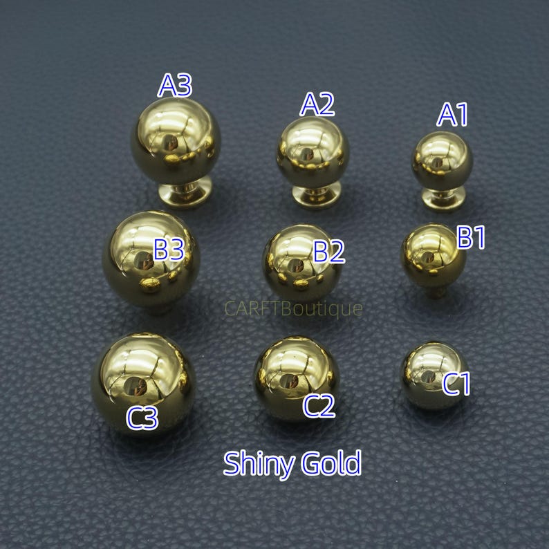 Puede incluir: Una colecci&oacute;n de pomos dorados brillantes para armarios de varios tama&ntilde;os. Los pomos tienen un dise&ntilde;o esf&eacute;rico con un v&aacute;stago y una base. El texto "Shiny Gold" se muestra en la parte inferior de la imagen. Los pomos est&aacute;n dispuestos en tres filas.