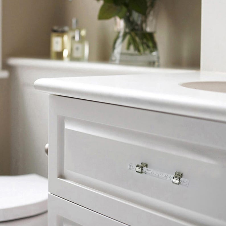 Peut inclure: Meuble-lavabo blanc avec une poign&eacute;e de tiroir en forme de cristal. Le meuble a un design &eacute;pur&eacute; et moderne avec une finition blanche lisse. La poign&eacute;e de tiroir est rectangulaire et a un aspect clair et textur&eacute;. Le meuble est dans une salle de bain.