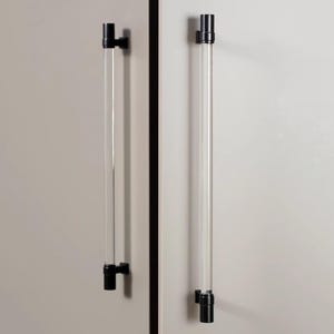 May include: Two cabinet pulls with a clear, cylindrical design and black hardware. The pulls are mounted on a light-colored cabinet door. The pulls are approximately 12 inches long.