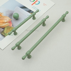 May include: Sage green cabinet hardware, including two long pulls and a round knob. The pulls are approximately 30 cm long, with decorative end details. The knob is a solid sphere. The hardware is displayed on a light background.