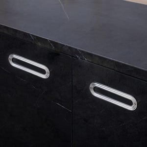 May include: A close-up of a black cabinet featuring two oval-shaped handles with silver rims. The cabinet has a dark, textured surface with white veining. The handles are positioned on the cabinet doors.